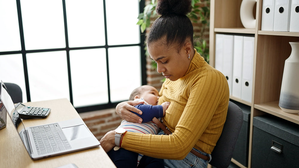 Black woman breastfeeding a baby while sitting at a work desk